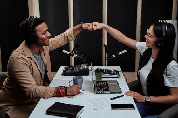 Two professionals shaking hands at a podcasting industry event, with microphones and branding visible in the background, signifying a successful networking interaction leading to potential interview opportunities.