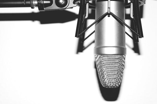 A close-up of a professional dynamic microphone, such as a Shure SM7B, positioned on a boom arm in front of a pop filter. The background is slightly blurred to focus on the microphone's components and build quality.